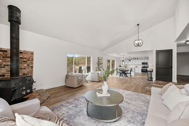 6712 C Highway 291, Nine Mile Falls, WA 99026 - living room with a chandelier, a wood stove, wood finished floors, baseboards, and high vaulted ceiling