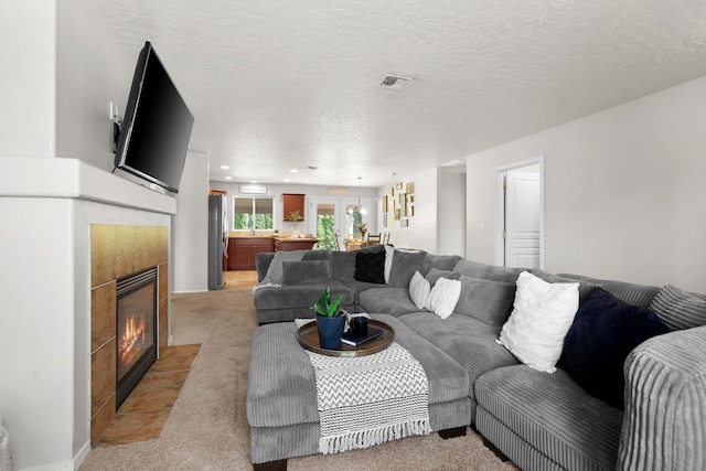 living area featuring visible vents, light carpet, recessed lighting, a tile fireplace, and a textured ceiling