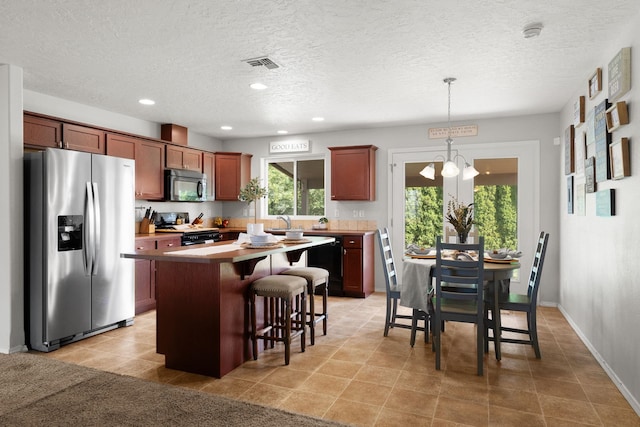 kitchen featuring visible vents, a kitchen island, an inviting chandelier, appliances with stainless steel finishes, and a kitchen bar