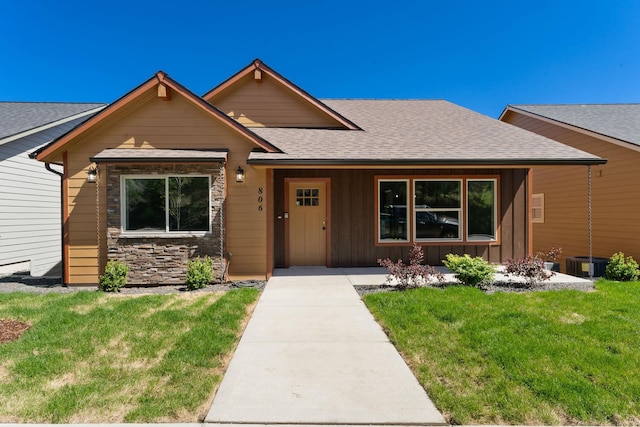 806 W Bolan Ave, Spokane, WA 99224 - view of front of property featuring a front yard, a shingled roof, stone siding, board and batten siding, and central AC unit