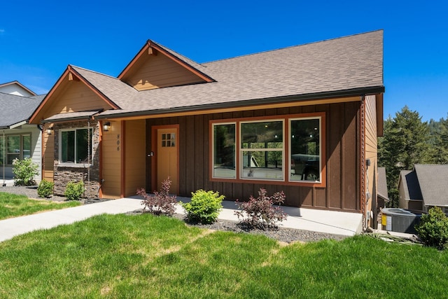 806 W Bolan Ave, Spokane, WA 99224 - view of front of house featuring a front yard, board and batten siding, roof with shingles, central AC, and stone siding