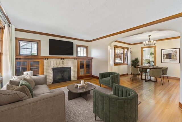living room featuring arched walkways, a chandelier, a brick fireplace, light wood-type flooring, and ornamental molding