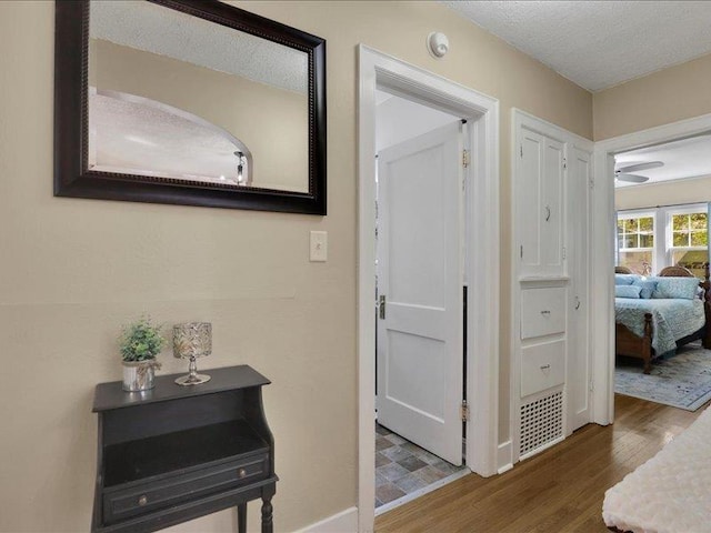 corridor featuring wood finished floors, a textured ceiling, and baseboards