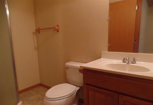 bathroom featuring a shower with door, vanity, baseboards, and toilet