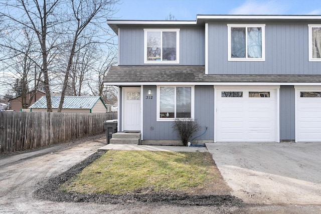 traditional-style home with an attached garage, fence, and a shingled roof