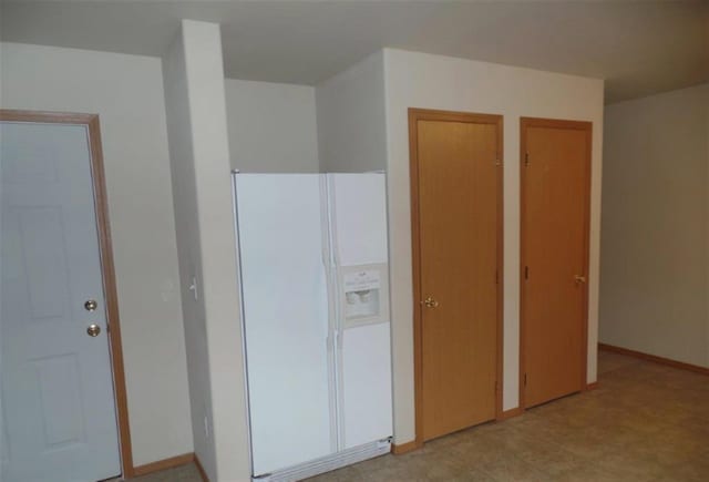 unfurnished bedroom with multiple closets, white refrigerator with ice dispenser, and baseboards