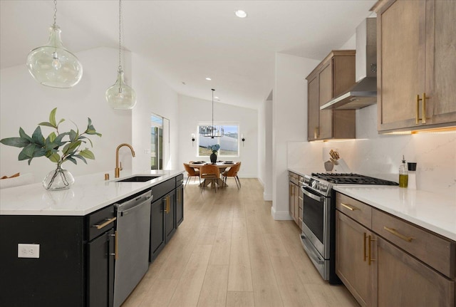 kitchen with stainless steel appliances, a sink, lofted ceiling, wall chimney range hood, and decorative light fixtures