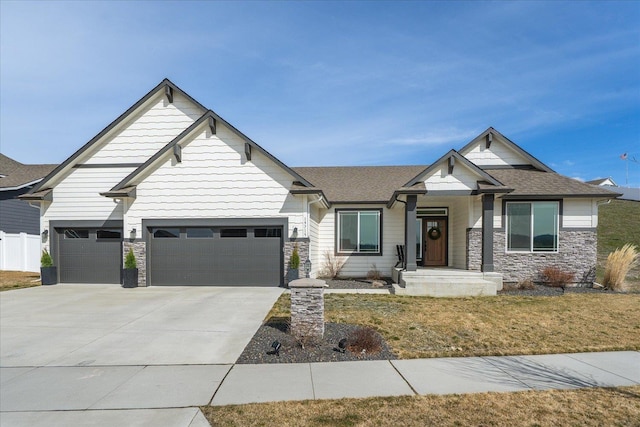craftsman inspired home featuring concrete driveway, stone siding, a shingled roof, a front yard, and a garage