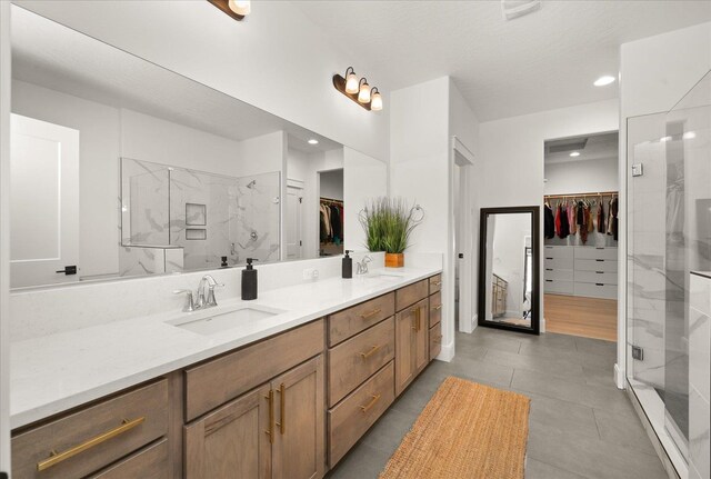 bathroom with double vanity, a spacious closet, a marble finish shower, and a sink
