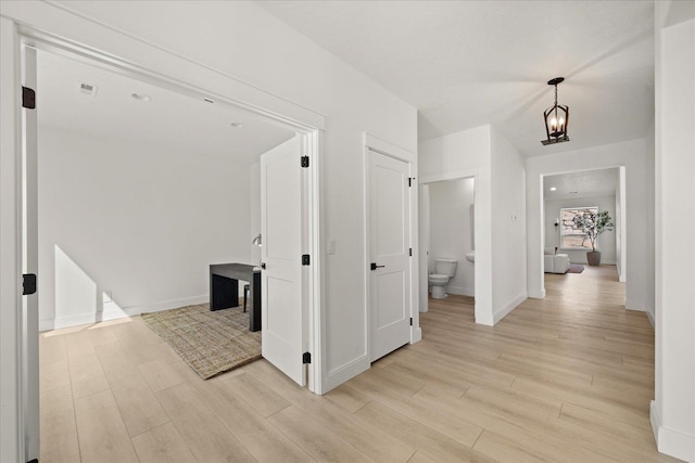hallway featuring baseboards, an inviting chandelier, visible vents, and light wood-type flooring