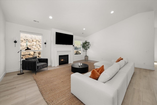 living room featuring a warm lit fireplace, light wood-style flooring, visible vents, and lofted ceiling