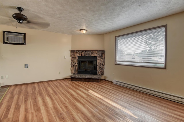 6208 N Wiscomb St, Spokane, WA 99208 - unfurnished living room featuring a baseboard radiator, a textured ceiling, wood finished floors, a stone fireplace, and a wall unit AC