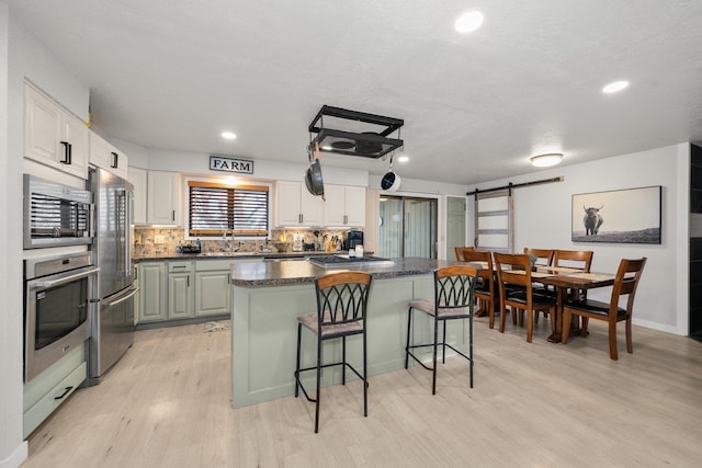 313 SE Trinity Ave, Wilbur, WA 99185 - kitchen with stainless steel appliances, light wood-type flooring, a barn door, a breakfast bar area, and dark countertops