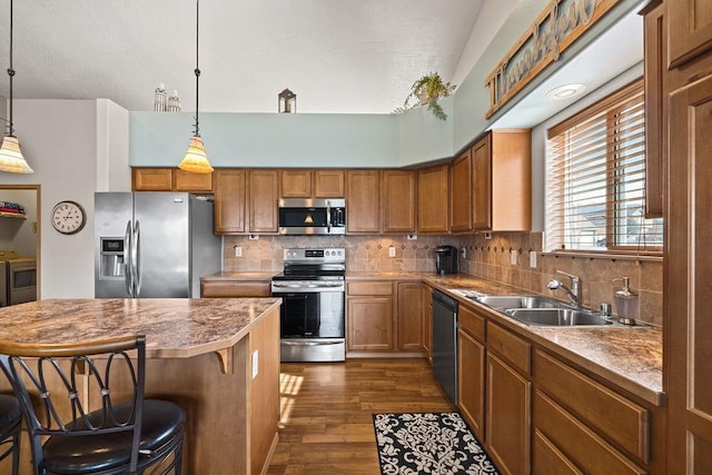 kitchen with dark wood-style floors, a kitchen bar, brown cabinets, a sink, and stainless steel appliances