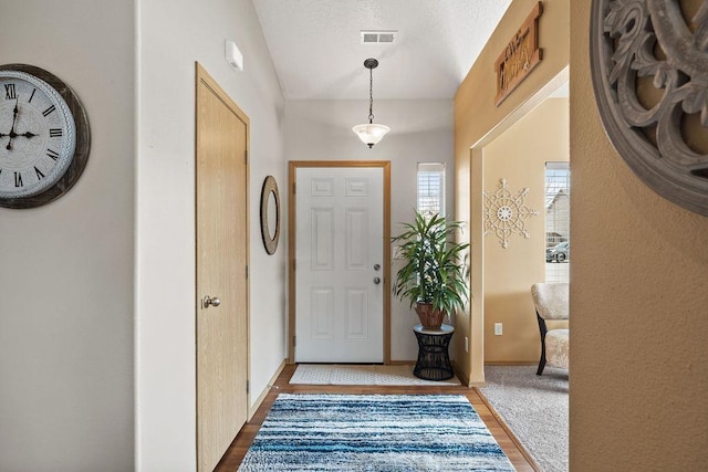foyer entrance featuring visible vents, baseboards, wood finished floors, and vaulted ceiling