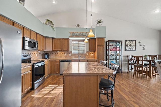 kitchen featuring brown cabinets, appliances with stainless steel finishes, a sink, high vaulted ceiling, and a kitchen bar