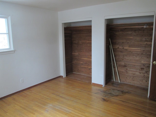 1914 W 8th Ave, Spokane, WA 99204 - unfurnished bedroom featuring baseboards, two closets, light wood-style floors, and wooden walls