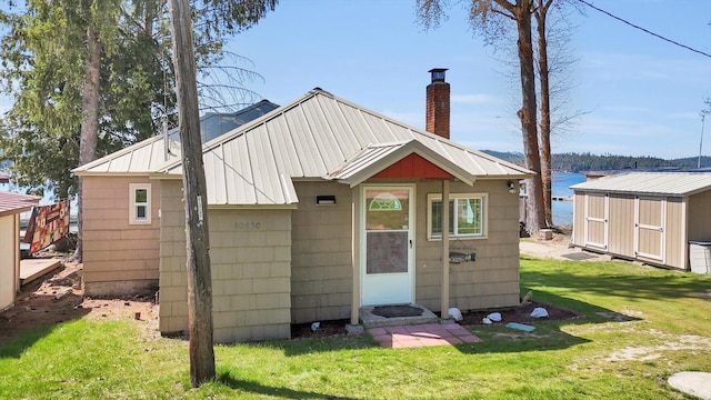 back of property featuring an outbuilding, a lawn, a storage unit, and a chimney