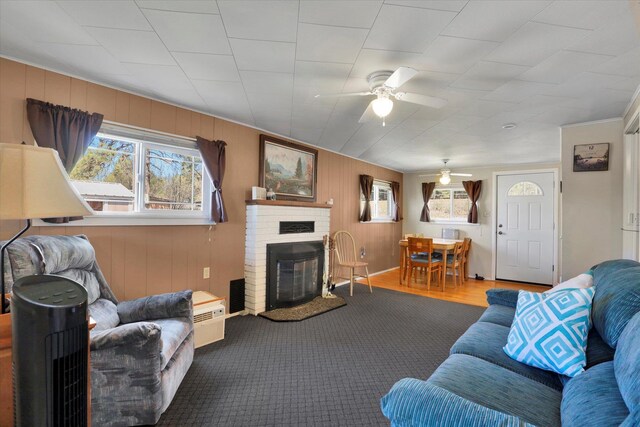living area featuring a brick fireplace, wooden walls, ceiling fan, and crown molding