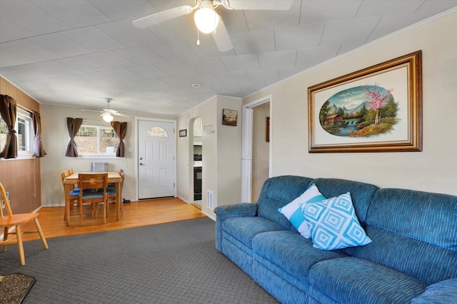 carpeted living room with ornamental molding, a ceiling fan, visible vents, and wood finished floors