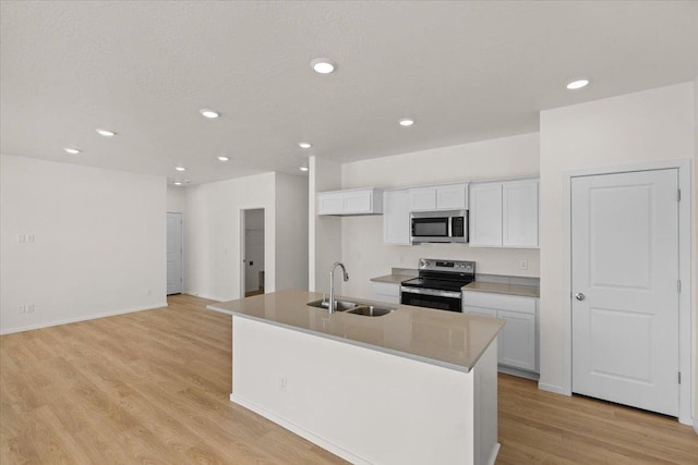 kitchen with light wood-type flooring, a sink, white cabinets, a kitchen island with sink, and appliances with stainless steel finishes