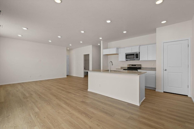 kitchen featuring white cabinetry, a center island with sink, a sink, light wood-style flooring, and appliances with stainless steel finishes