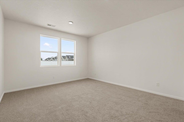 carpeted spare room with a textured ceiling, baseboards, and visible vents