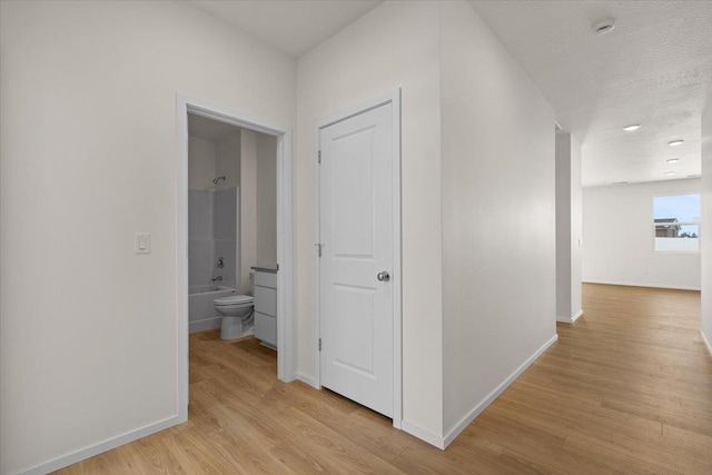 hallway featuring baseboards, a textured ceiling, and light wood finished floors