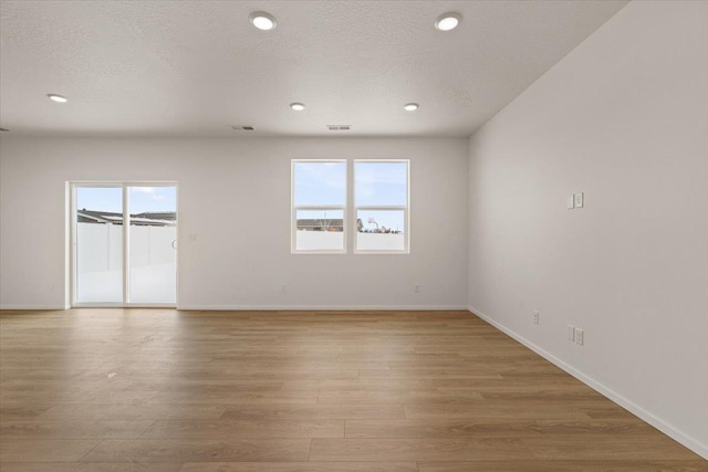 spare room featuring a textured ceiling, a healthy amount of sunlight, and light wood-type flooring