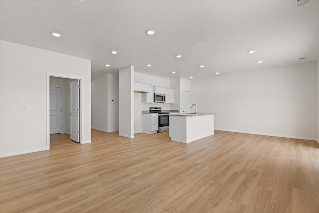 unfurnished living room with recessed lighting, light wood-type flooring, baseboards, a textured ceiling, and a sink