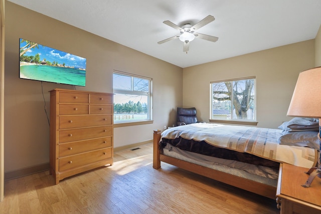 bedroom with baseboards, ceiling fan, multiple windows, and light wood-type flooring