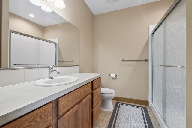 bathroom featuring stone finish floor, baseboards, toilet, vanity, and a stall shower