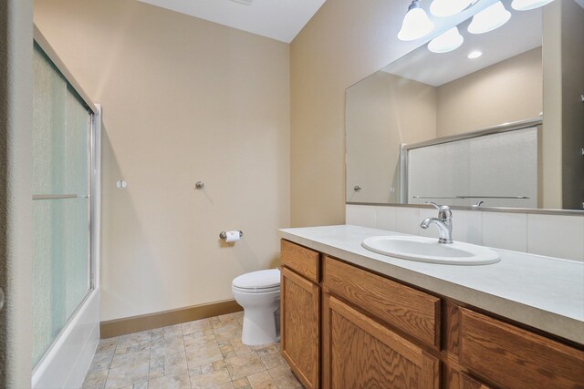 bathroom featuring stone finish floor, baseboards, toilet, vanity, and enclosed tub / shower combo