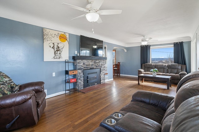 living area with a stone fireplace, arched walkways, wood finished floors, and ceiling fan