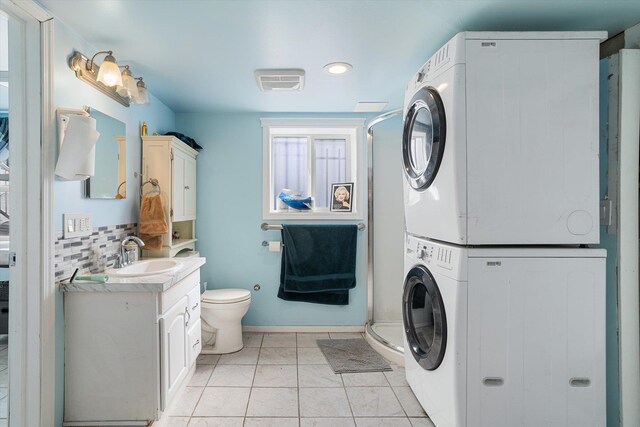 clothes washing area with baseboards, a sink, light tile patterned flooring, stacked washer / dryer, and laundry area