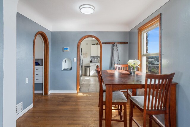 dining room featuring baseboards, arched walkways, washer / dryer, visible vents, and wood finished floors