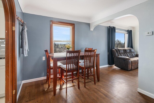 dining space featuring arched walkways, hardwood / wood-style flooring, and baseboards