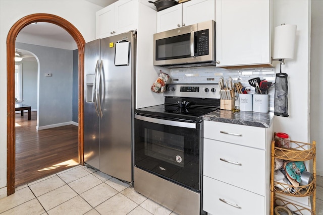 kitchen featuring light tile patterned floors, stainless steel appliances, white cabinets, arched walkways, and decorative backsplash