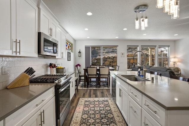 kitchen with stainless steel appliances, dark countertops, dark wood-type flooring, a sink, and backsplash