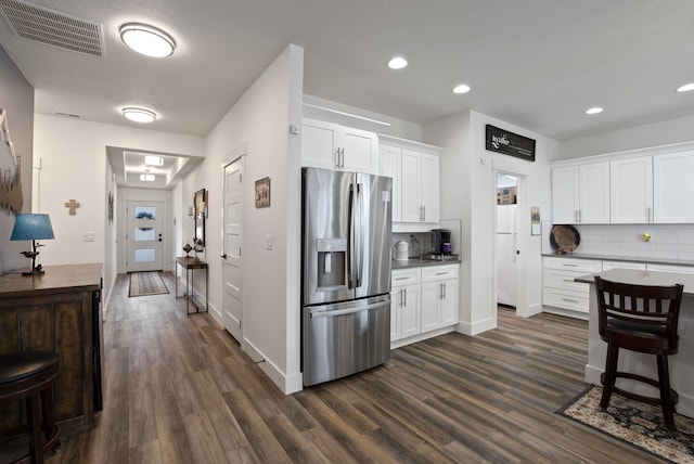 kitchen featuring stainless steel fridge, dark wood-style flooring, backsplash, visible vents, and white cabinets