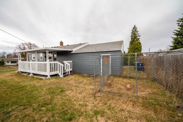back of property with a deck, a chimney, a shingled roof, a lawn, and fence