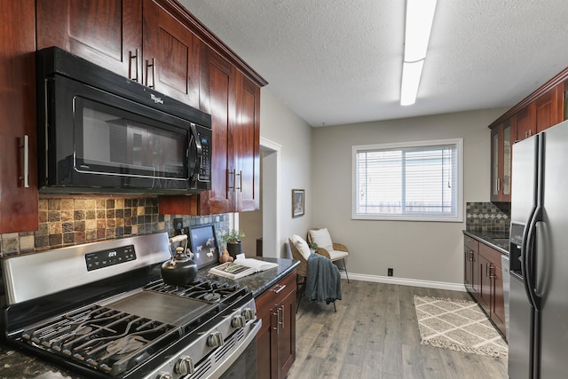 kitchen featuring dark stone counters, a sink, dark wood-type flooring, backsplash, and appliances with stainless steel finishes