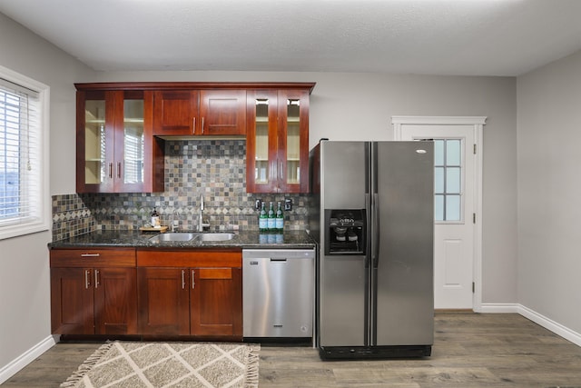 kitchen with tasteful backsplash, dark stone counters, light wood-style floors, appliances with stainless steel finishes, and a sink