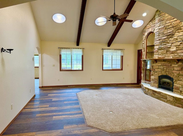 unfurnished living room with a stone fireplace, wood finished floors, arched walkways, and a ceiling fan