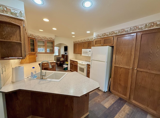 kitchen featuring light countertops, a peninsula, white appliances, arched walkways, and a sink