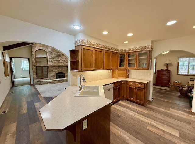 kitchen featuring a peninsula, brown cabinets, arched walkways, a sink, and white dishwasher
