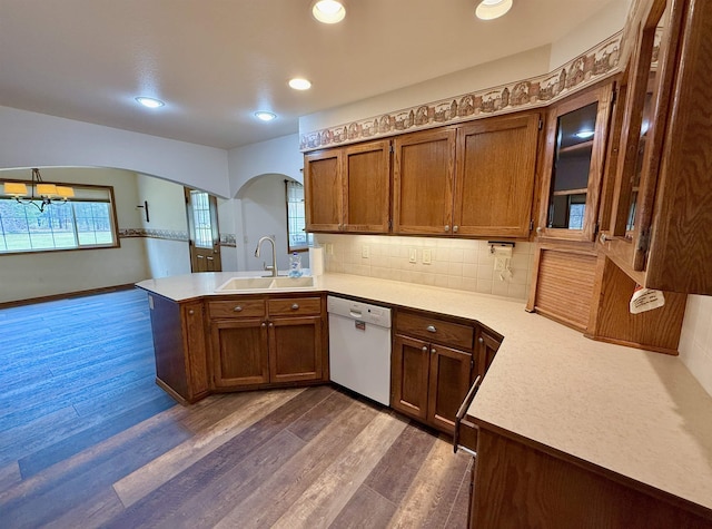 kitchen with light countertops, a sink, arched walkways, a peninsula, and white dishwasher
