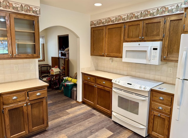 kitchen with light countertops, white appliances, dark wood-type flooring, arched walkways, and brown cabinetry