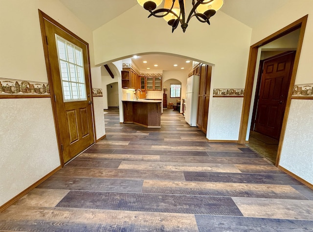interior space featuring a sink, dark wood finished floors, lofted ceiling, arched walkways, and an inviting chandelier