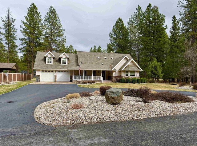 view of front of house featuring covered porch, aphalt driveway, fence, and an attached garage